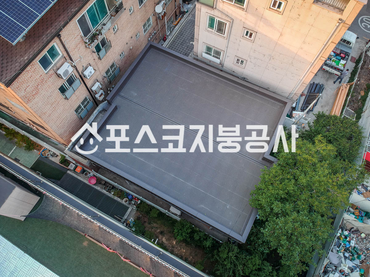 양옆 건물이 바짝 붙은 평지붕 옥상 전체를 칼라강판으로 덮은 모습